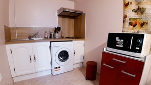 A compact kitchen with a washing machine, a microwave, and a red cabinet. - 2 steps from the historic center, gite*** with beautiful saltwater swimming pool (Sarlat-la-Canéda)