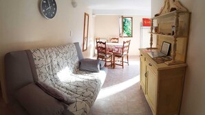 A living room with a sofa, a wooden cabinet, and a dining area with a table and chairs. - 2 steps from the historic center, gite*** with beautiful saltwater swimming pool (Sarlat-la-Canéda)