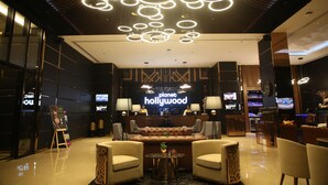 A lobby with a modern design, featuring a central seating area, a reception desk, and multiple screens displaying content. - Planet Hollywood (Thane)