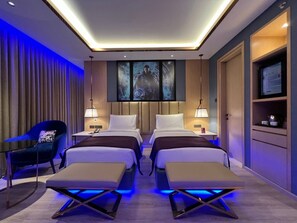 A modern hotel room with two beds, a desk, a chair, and a TV. - Planet Hollywood (Thane)