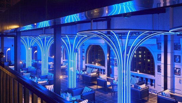 A modern lounge area with seating and tables, illuminated by blue neon lights, and featuring arched architectural elements. - Planet Hollywood (Thane)