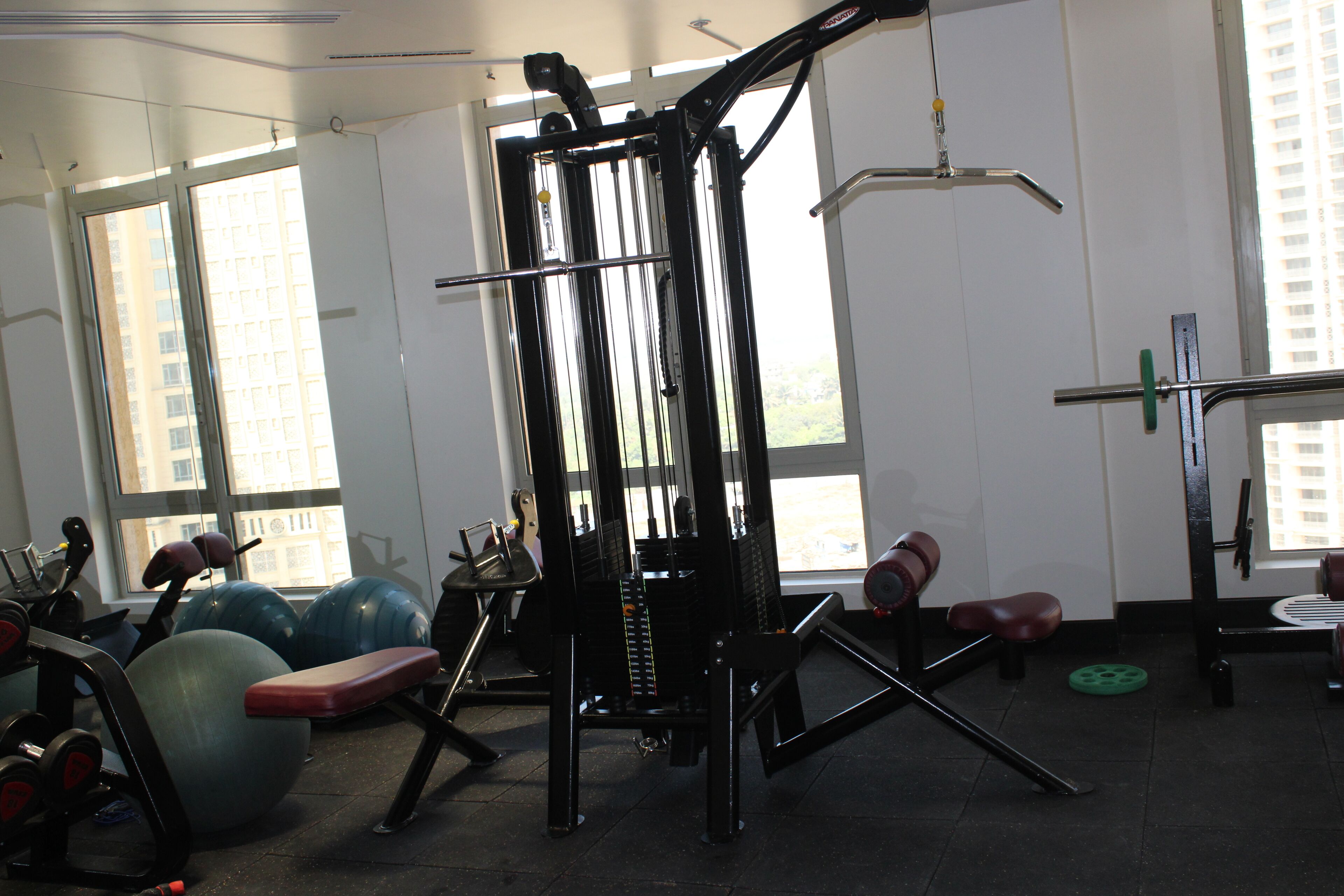Une salle de sport équipée de matériel d’exercice, dotée de grandes fenêtres et offrant une vue sur les bâtiments environnants.