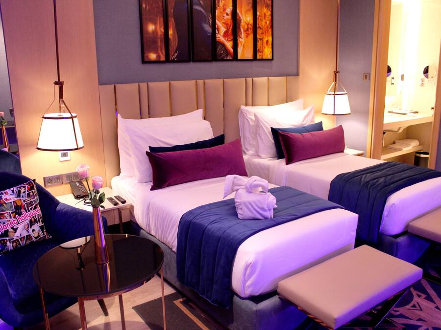 Een hotelkamer met twee bedden, een tafeltje, een stoel en een nachtkastje met een lamp.