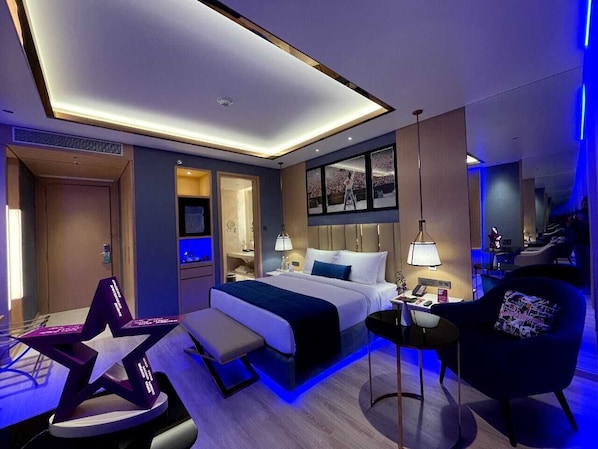 A modern hotel room with a large bed, bedside tables, a desk, and a seating area with a chair and bench.