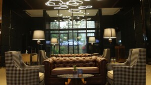 A lobby with a modern chandelier, leather sofa, houndstooth chairs, and a marble floor. - Planet Hollywood (Thane)