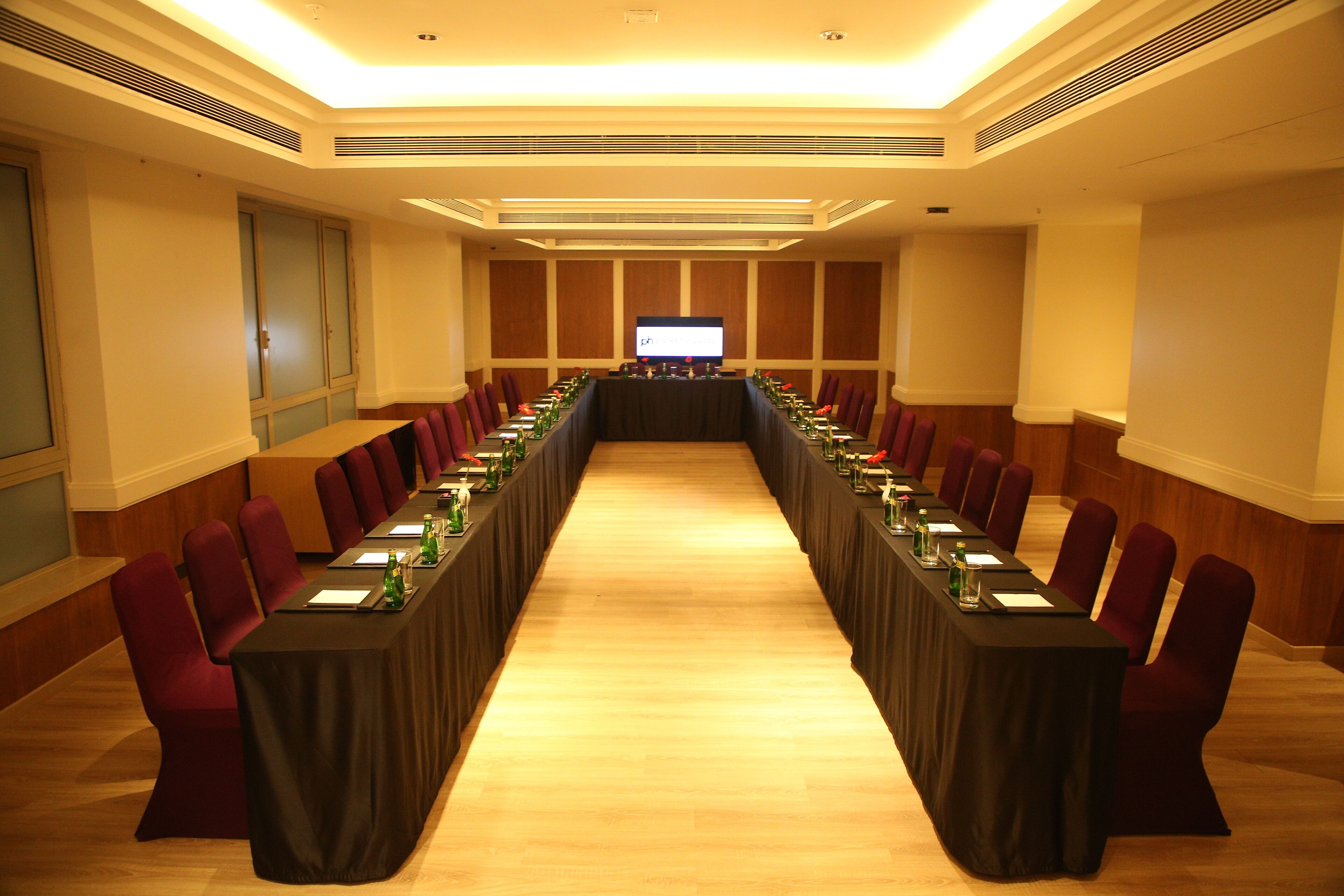 Un salón de conferencias con una larga mesa, sillas rojas y una pantalla grande al frente.