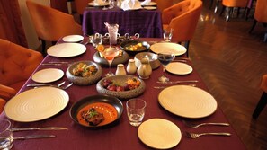 A dining table set with plates, bowls, glasses, and cutlery, surrounded by orange chairs. - Planet Hollywood (Thane)