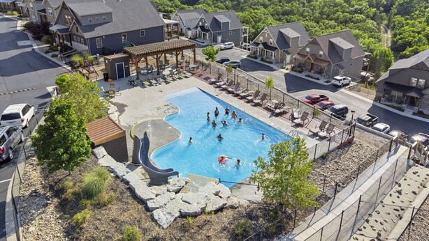 A residential area with a swimming pool surrounded by houses, a covered patio, and a view of a lake. - Private Basketball Court/Hot Tub-Community Pools (Branson)