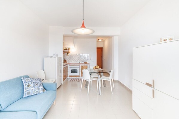 A modern kitchen with white cabinets, a dining table with chairs, and a blue sofa with patterned cushions.