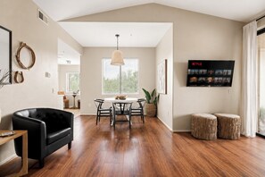 Un vaste salon doté d’un parquet, d’un canapé en cuir noir, d’une table à manger avec des chaises, d’un luminaire suspendu et d’un téléviseur fixé au mur, sur lequel est diffusé Netflix.
