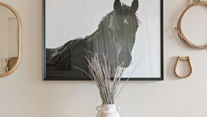 Ett rum med två svarta lädersoffor, ett träbord, en vas med torkade växter och ett inramat porträtt av en häst på väggen.