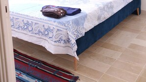 Une chambre avec une tête de lit bleue, un lit recouvert d’une couvre-lit à motifs blancs et bleus, et un tableau abstrait bleu accroché au mur.