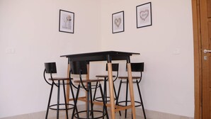 Un coin repas avec une table noire et quatre chaises, chacune dotée d’un siège en bois et d’une structure en métal noir. Trois tableaux encadrés sont accrochés au mur au-dessus de la table.