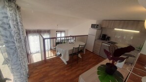 A spacious room with a wooden floor, a dining table with chairs, a kitchen area with a microwave and refrigerator, and a balcony with a view.