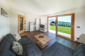 A modern living room with a sofa, a coffee table, and a sliding glass door leading to a balcony with a view of the mountains. - Holiday Apartment Avea App 2 with Mountain View and Garden (Laion)
