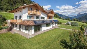 Une maison à deux étages avec un balcon, un jardin et une vue sur les montagnes.