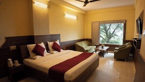 A hotel room with a large bed, a chair, a small table, and a TV. - Hotel Falcon Crest (Kandaghat)