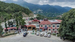 A hotel with a red roof and multiple buildings, surrounded by lush greenery and mountains. - Hotel Falcon Crest (Kandaghat)