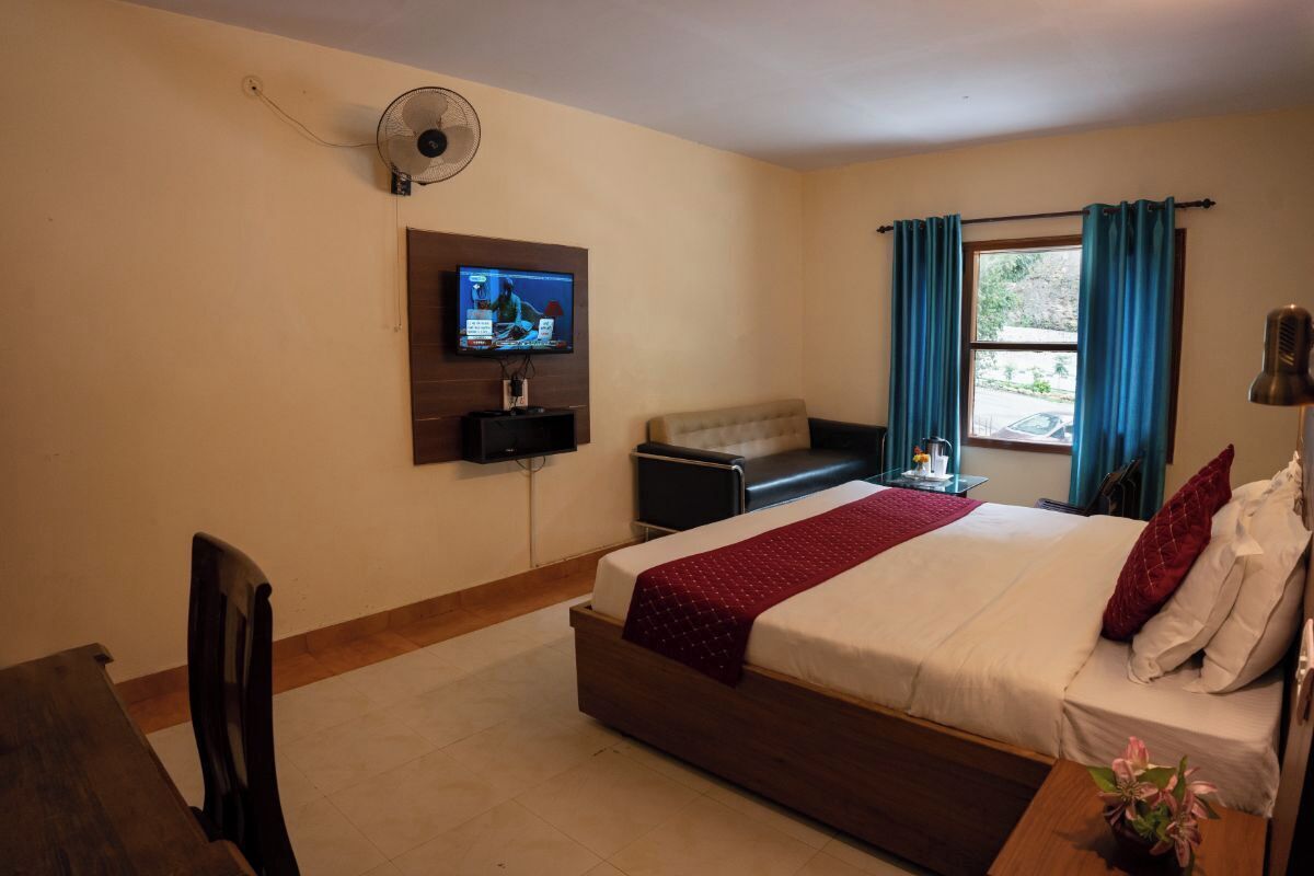 Ein Hotelzimmer mit Bett, Wand-Fernseher, Schreibtisch und einem Fenster mit Vorhängen.