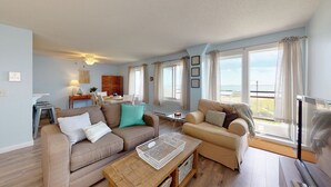 A living room with a sofa, armchair, and coffee table. There is a dining area with a table and chairs. Large windows provide a view of the outdoors. - Oceanview Oasis by Bayley Vacation Rentals (Old Orchard Beach)