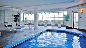 A modern indoor pool area with lounge chairs, a small table, and large windows offering a view of the outdoors. - Oceanview Oasis by Bayley Vacation Rentals (Old Orchard Beach)