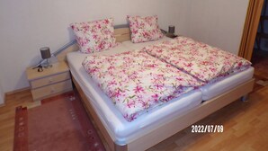 A double bed with floral bedding, a bedside table with a lamp, and a wall-mounted picture.