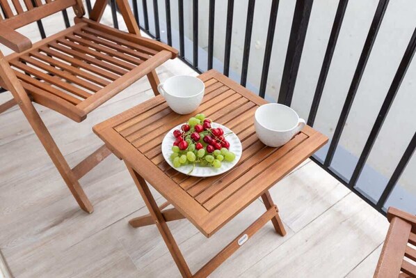 A wooden table with a plate of fruit and two white cups on a balcony.