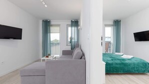 En modern lägenhet med en grå soffa, en grön säng och en tv som är monterad på väggen.