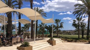Outdoor seating with umbrellas, palm trees, and a view of a golf course. - Holiday Home "Los Almendros" with Shared Pool, Terrace & Wi-Fi (Vera)