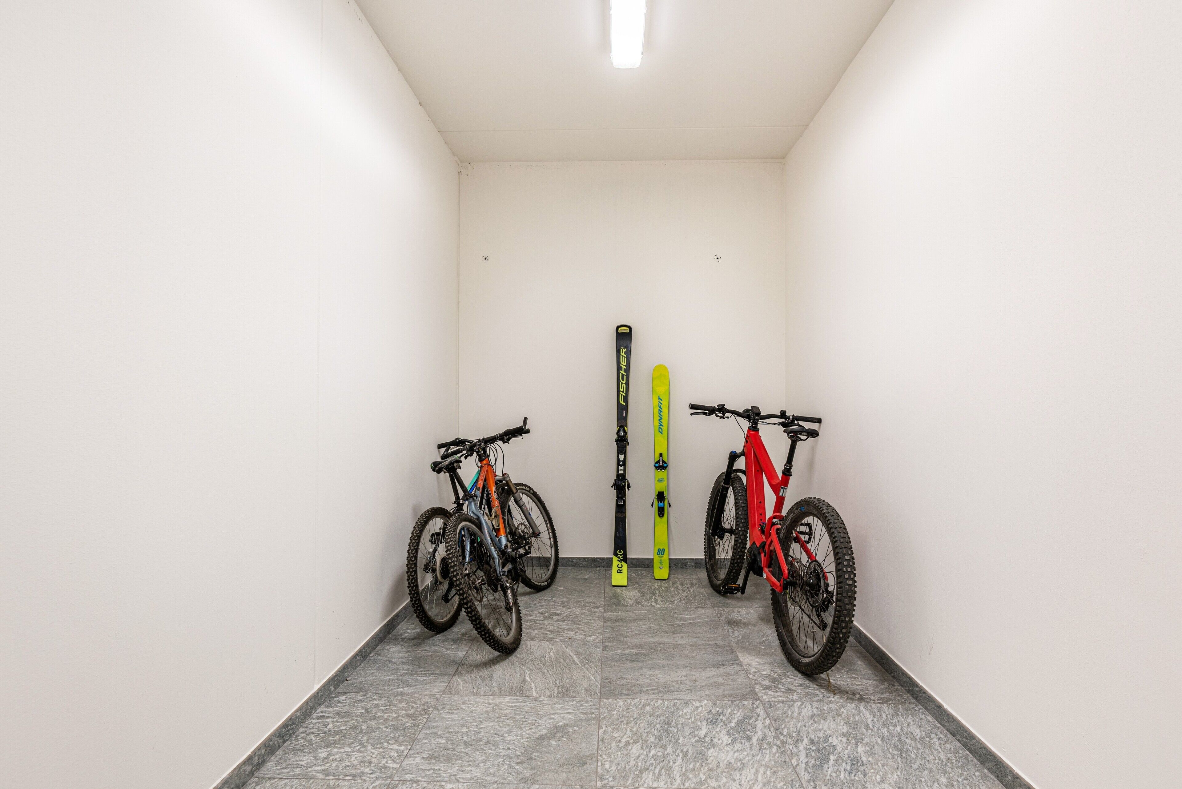 Un couloir étroit dans lequel sont appuyés contre le mur deux vélos et deux paires de skis.
