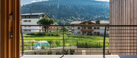A view from a balcony with a mountain backdrop, a green field, and buildings.