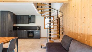 Eine moderne Küche mit dunklen Schränken, einer Holztreppe, einem grauen Sofa und einem Holzessttisch.