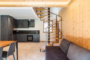 Une cuisine moderne avec des meubles de couleur sombre, un escalier en bois, un canapé gris et une table à manger en bois.