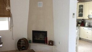 A room with a fireplace, a table, and a kitchen area with cabinets and appliances. - Pet-Friendly Villa Casa Cuesta with Pool & Garden (Bolnuevo)