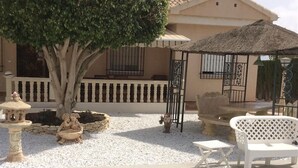 A patio area with a thatched roof, white outdoor furniture, and decorative stone elements. - Pet-Friendly Villa Casa Cuesta with Pool & Garden (Bolnuevo)