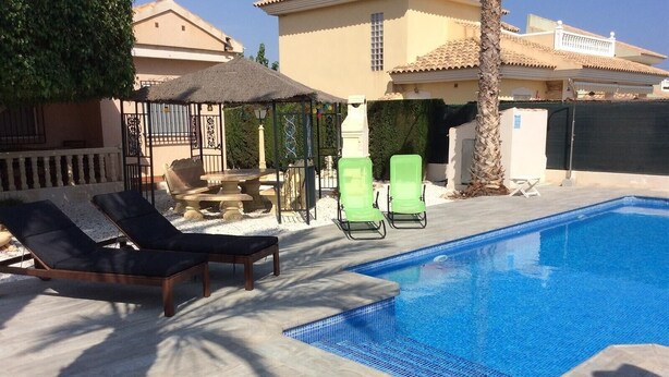 A swimming pool with lounge chairs, a pergola, and a stone table. - Pet-Friendly Villa Casa Cuesta with Pool & Garden (Bolnuevo)
