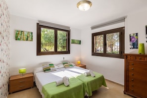 Une chambre avec deux lits, une commode en bois, une table de chevet avec une lampe et des œuvres d’art accrochées aux murs.