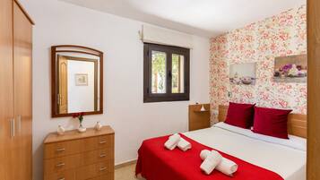 Une chambre à coucher avec un lit, une commode, un miroir, une fenêtre et un papier peint à motifs floraux.