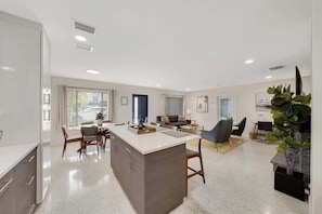 Una cocina moderna con una isla central, comedor con sillas y sala de estar con sofá y mesa de centro.