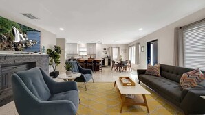 Una sala moderna con sofá, sillón y mesa de centro, una cocina al fondo y una chimenea.