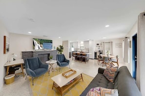 A modern living room with a sofa, armchairs, a coffee table, and a dining area with a table and chairs.