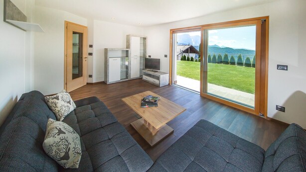 Un salon moderne avec un canapé, une table basse et une porte-fenêtre coulissante donnant sur un balcon d’où l’on peut admirer la vue sur les montagnes.