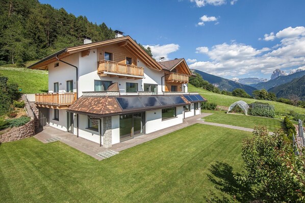 A two-story house with a balcony, a garden, and a view of mountains.