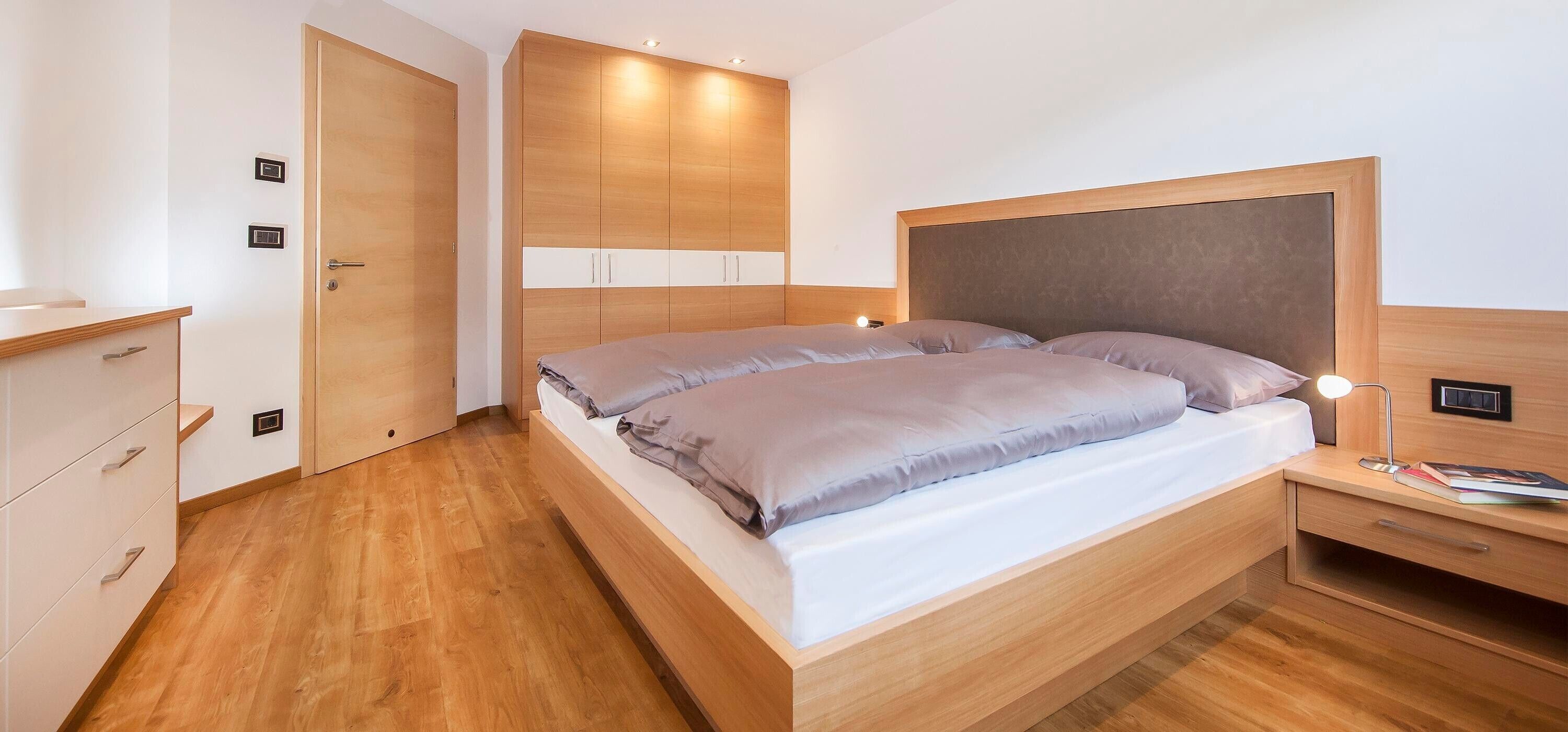 A modern bedroom with a wooden bed, bedside tables, a wardrobe, and built-in lighting.