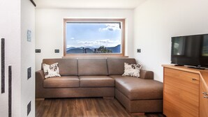 Un sofá de cuero marrón con cojines estampados, un armario de madera, un televisor y una ventana con vista a la montaña.