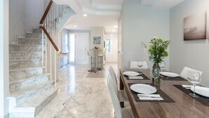 Une salle à manger spacieuse avec un escalier en marbre, une table à manger en bois dressée pour quatre personnes et une vue sur le salon attenant.