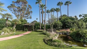 Un jardin aménagé avec des allées, des palmiers et un petit étang.