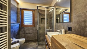 Een moderne badkamer met een douchecabine van glas, een houten wastafelmeubel, een toilet en een bidet.