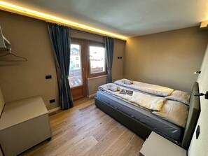 A compact room with a bed, a desk, and a window with curtains.