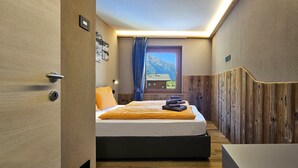 Een slaapkamer met een bed, houten lambrisering, een raam met uitzicht op bergen en een deur met slot.